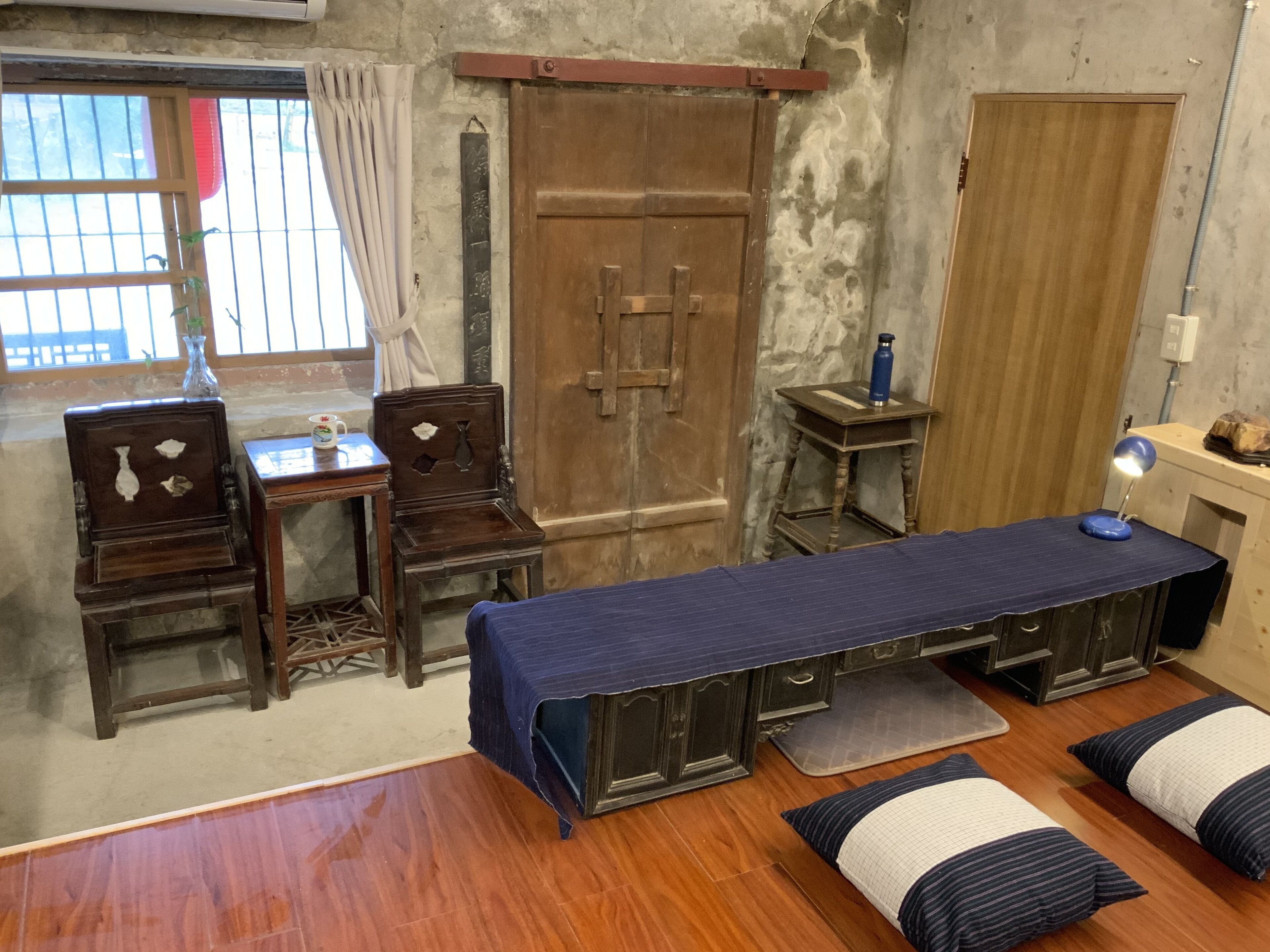 Um quarto japonês tradicional com piso de tatame, uma cama de madeira baixa, uma escrivaninha com cadeira, um armário de madeira e uma mesinha com abajur.