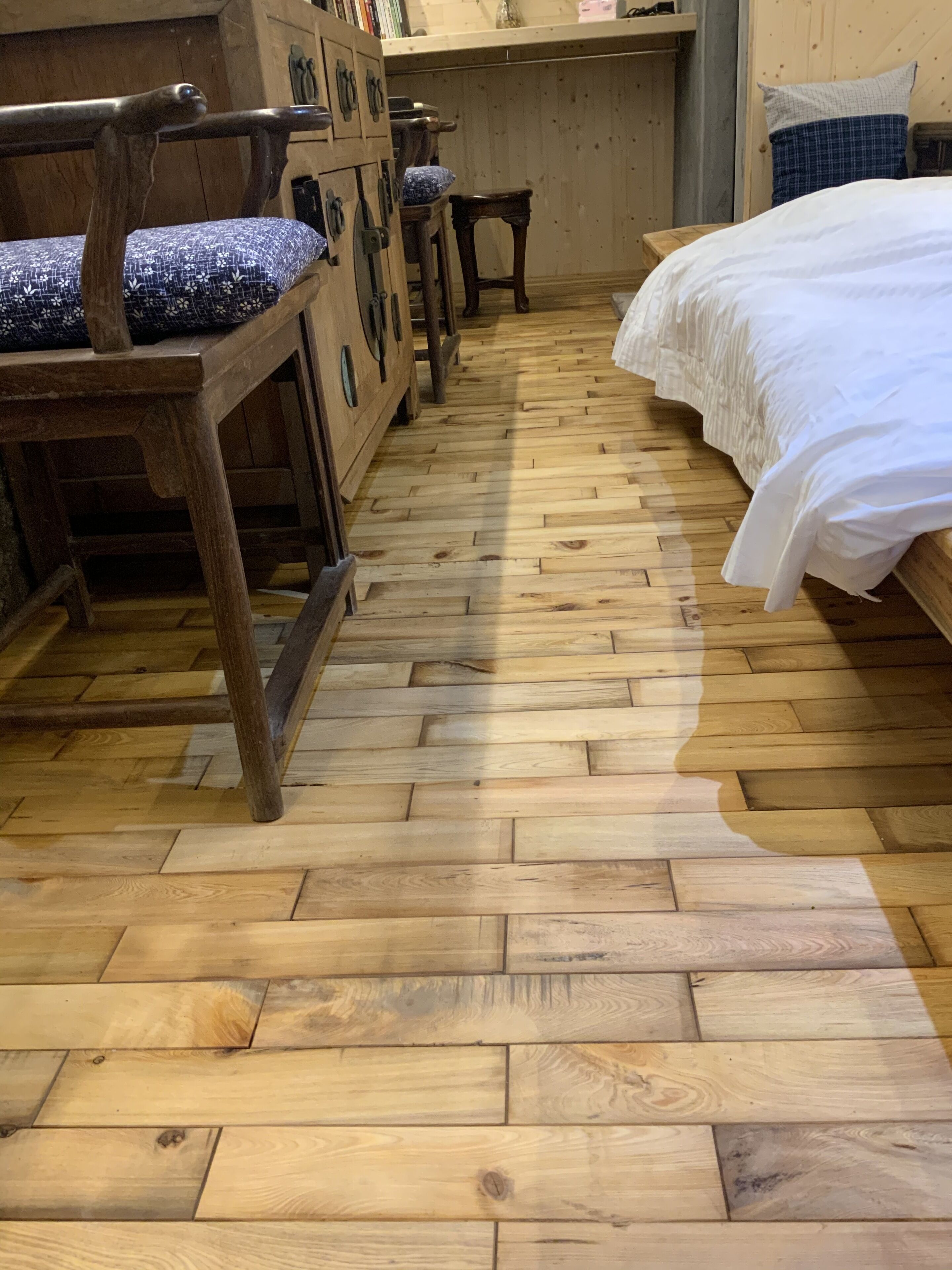 Suelo de madera con un estampado de cenefa, cama con ropa de cama blanca y muebles de madera con cojines azules.