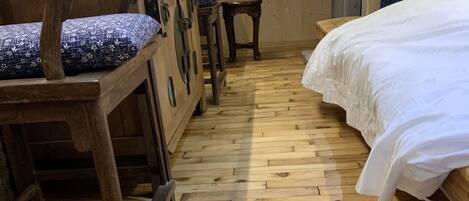 Suelo de madera con un estampado de cenefa, cama con ropa de cama blanca y muebles de madera con cojines azules.