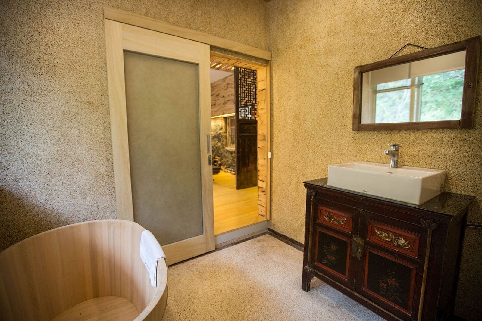 A bathroom with a wooden bathtub, a white sink, and a wooden cabinet with decorative carvings.