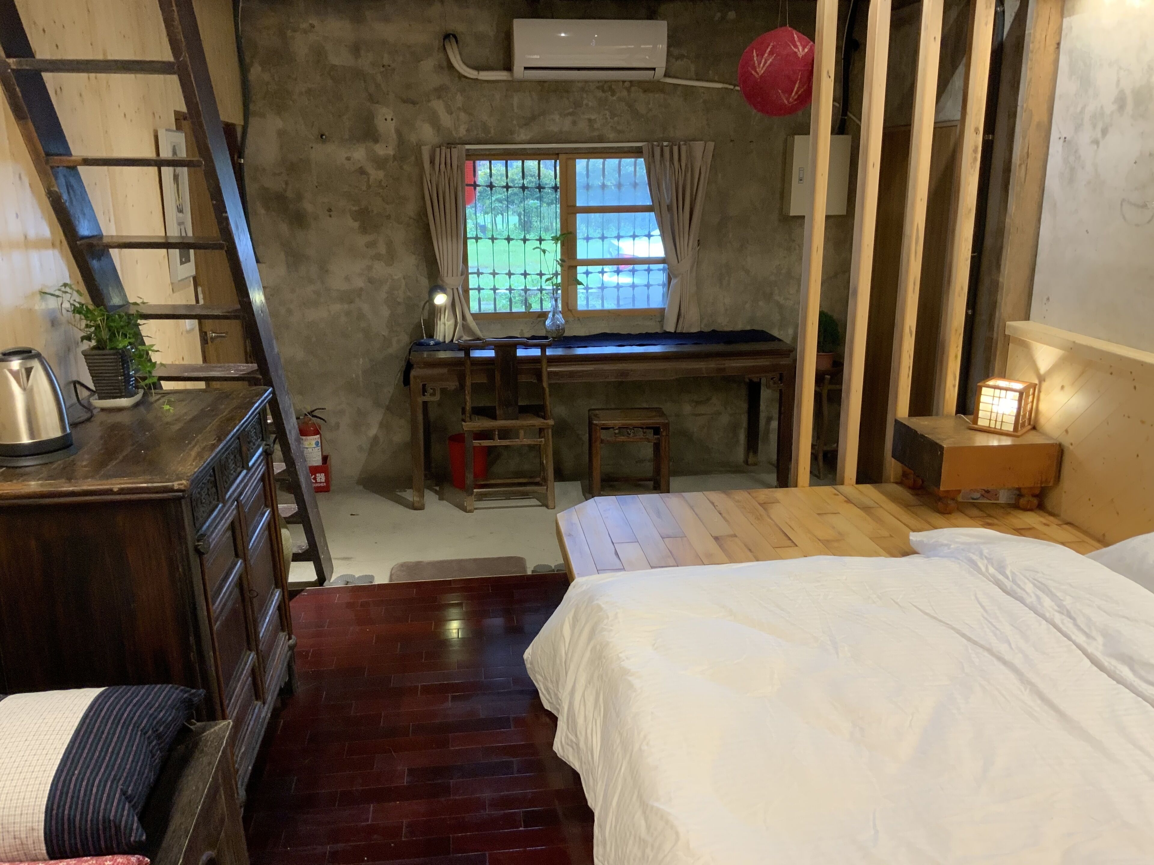 A compact room with a wooden desk, a bed, and a small stool.