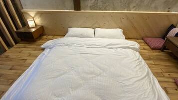 Una cama de madera con ropa de cama blanca en una habitación con pared de hormigón y suelo de madera.