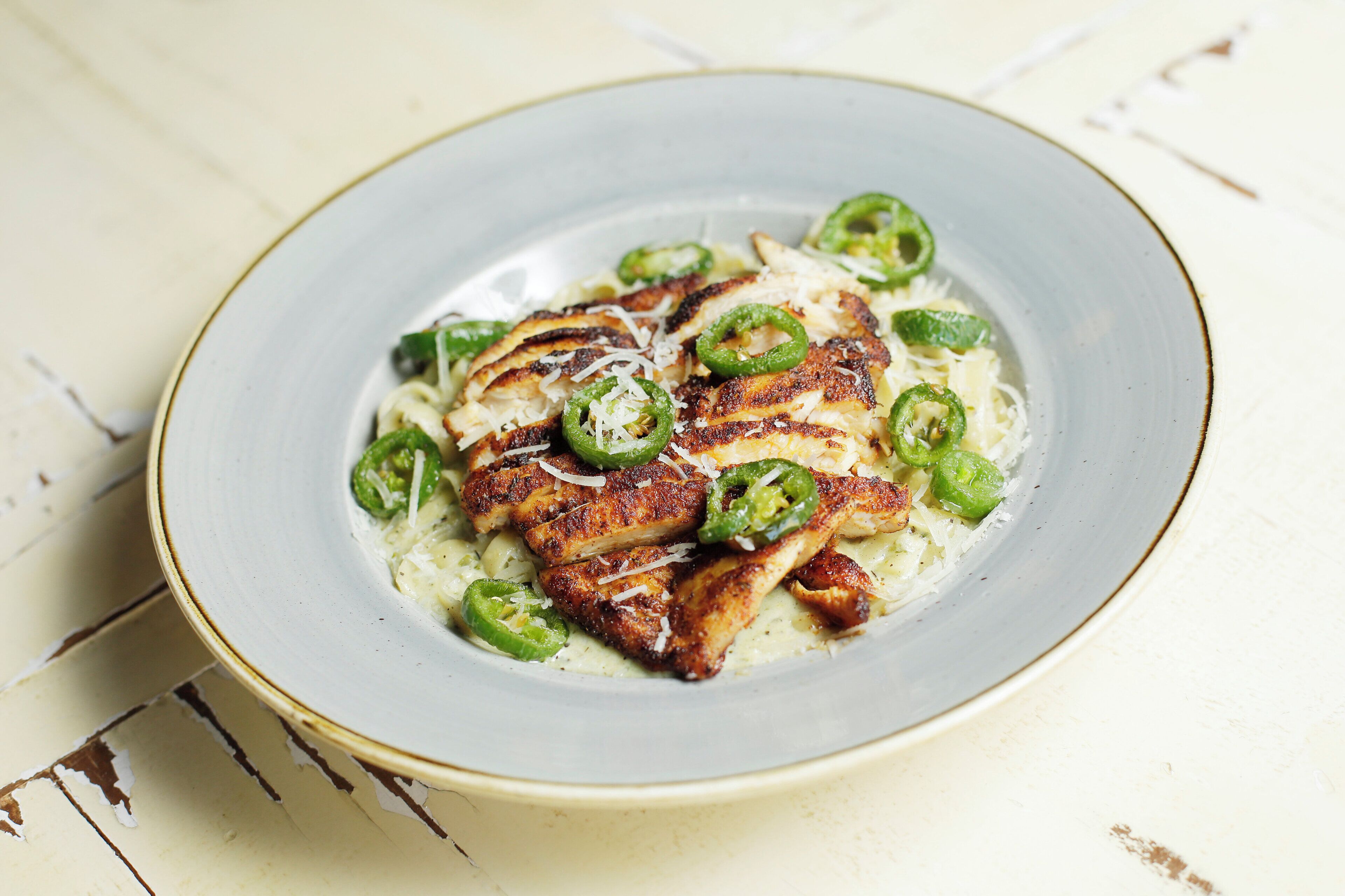 A plate of grilled chicken with green peppers and cheese on a white plate.