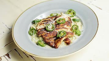 A plate of grilled chicken with green peppers and cheese on a white plate.