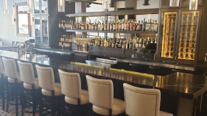 A bar area with a long counter, multiple stools, and shelves stocked with bottles. - Hotel Indigo Spokane Downtown by IHG (Spokane)