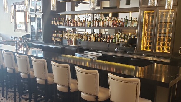 A bar area with a long counter, multiple stools, and shelves stocked with bottles. - Hotel Indigo Spokane Downtown by IHG (Spokane)