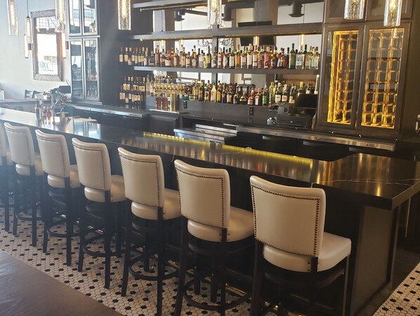 A bar area with a long counter, multiple stools, and shelves stocked with bottles. - Hotel Indigo Spokane Downtown by IHG (Spokane)