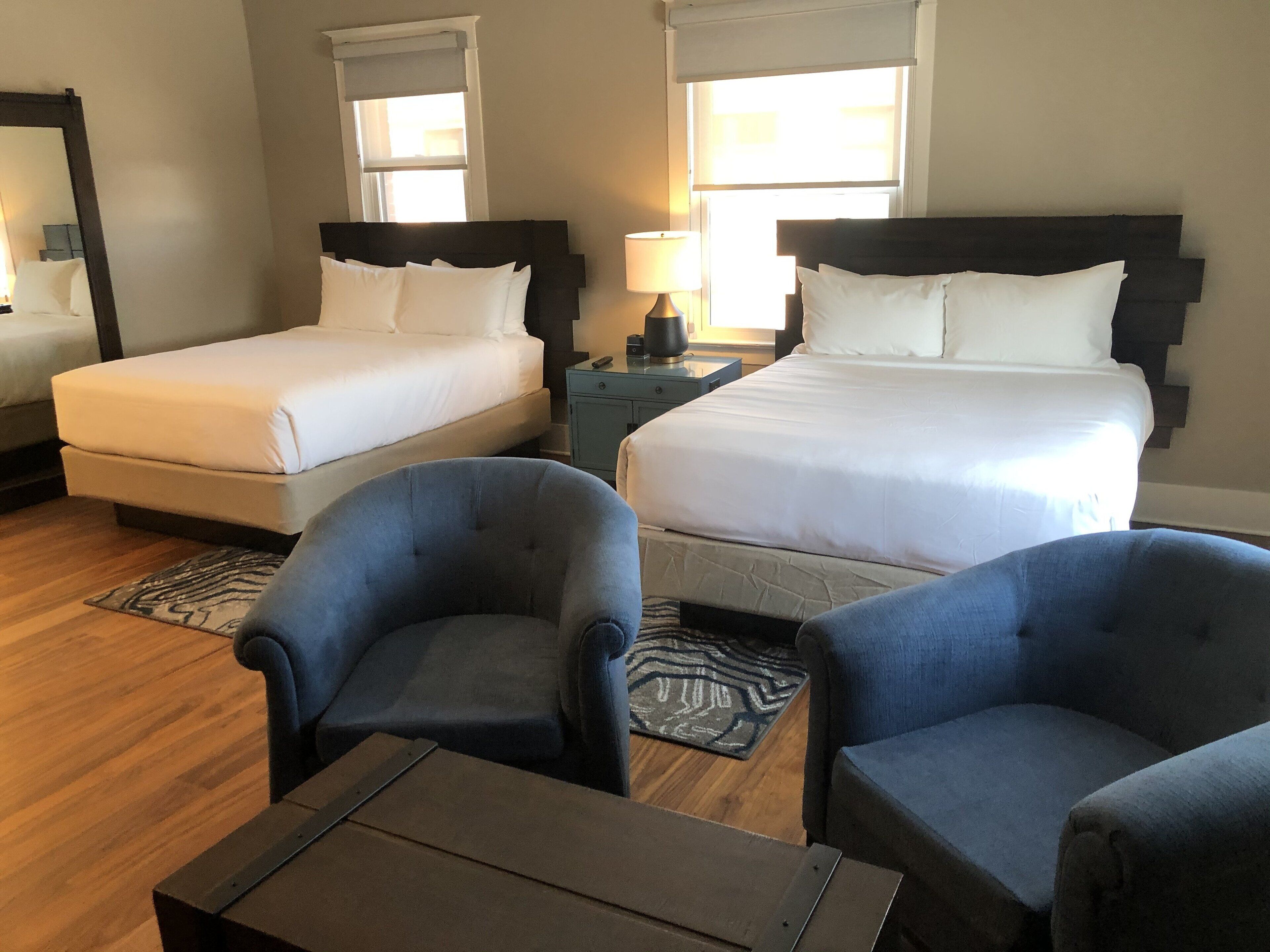 A hotel room with two beds, a desk, two armchairs, and a small table.