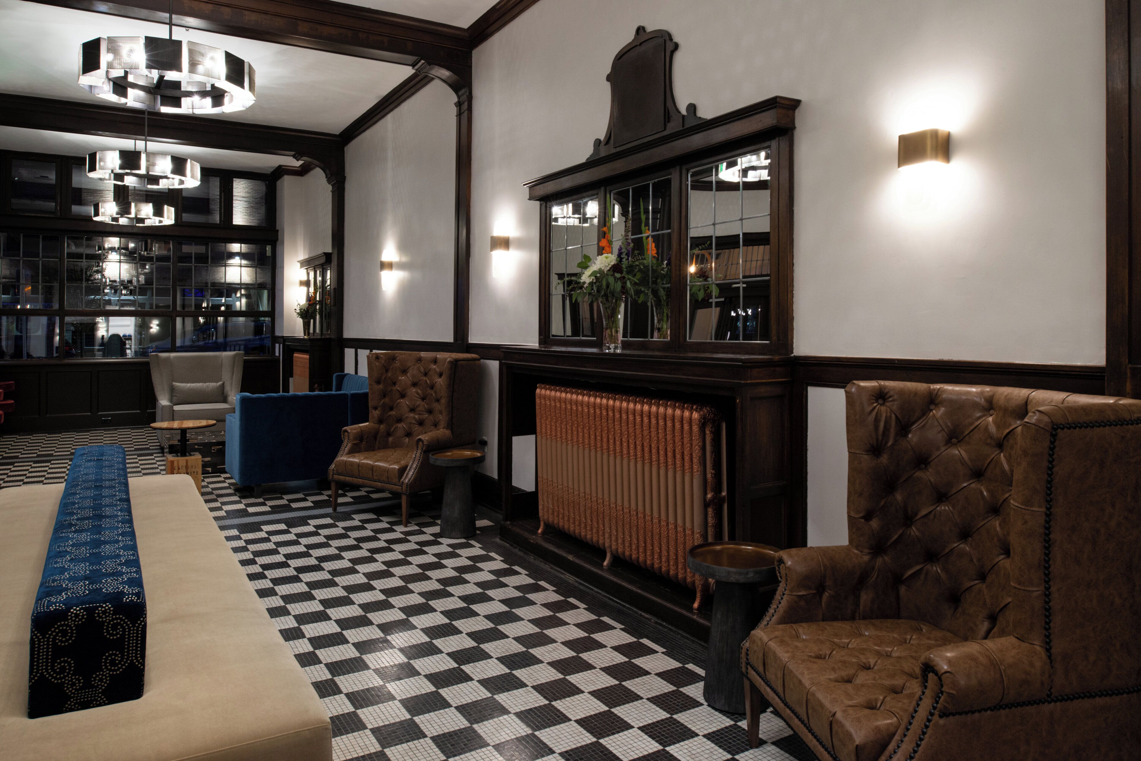 Een hotellobby met een zwart-wit betegelde vloer, leren fauteuils, een blauwe bank, een houten salontafel en een lange bank.