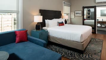 A hotel room with a bed, a blue sofa, a nightstand with a lamp, a patterned rug, and a window with a view.