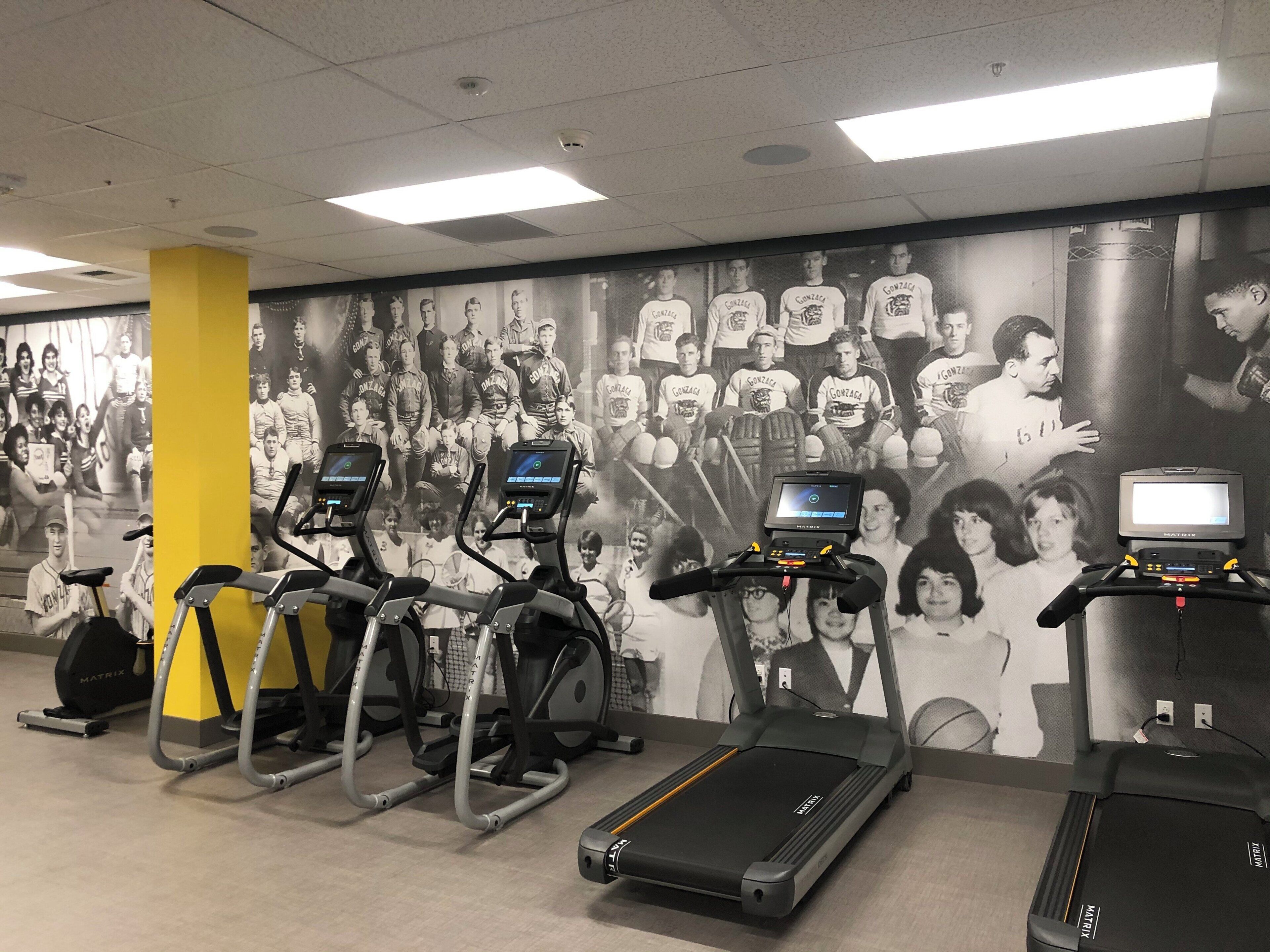 A gym with treadmills, stationary bikes, and a wall of team photos.