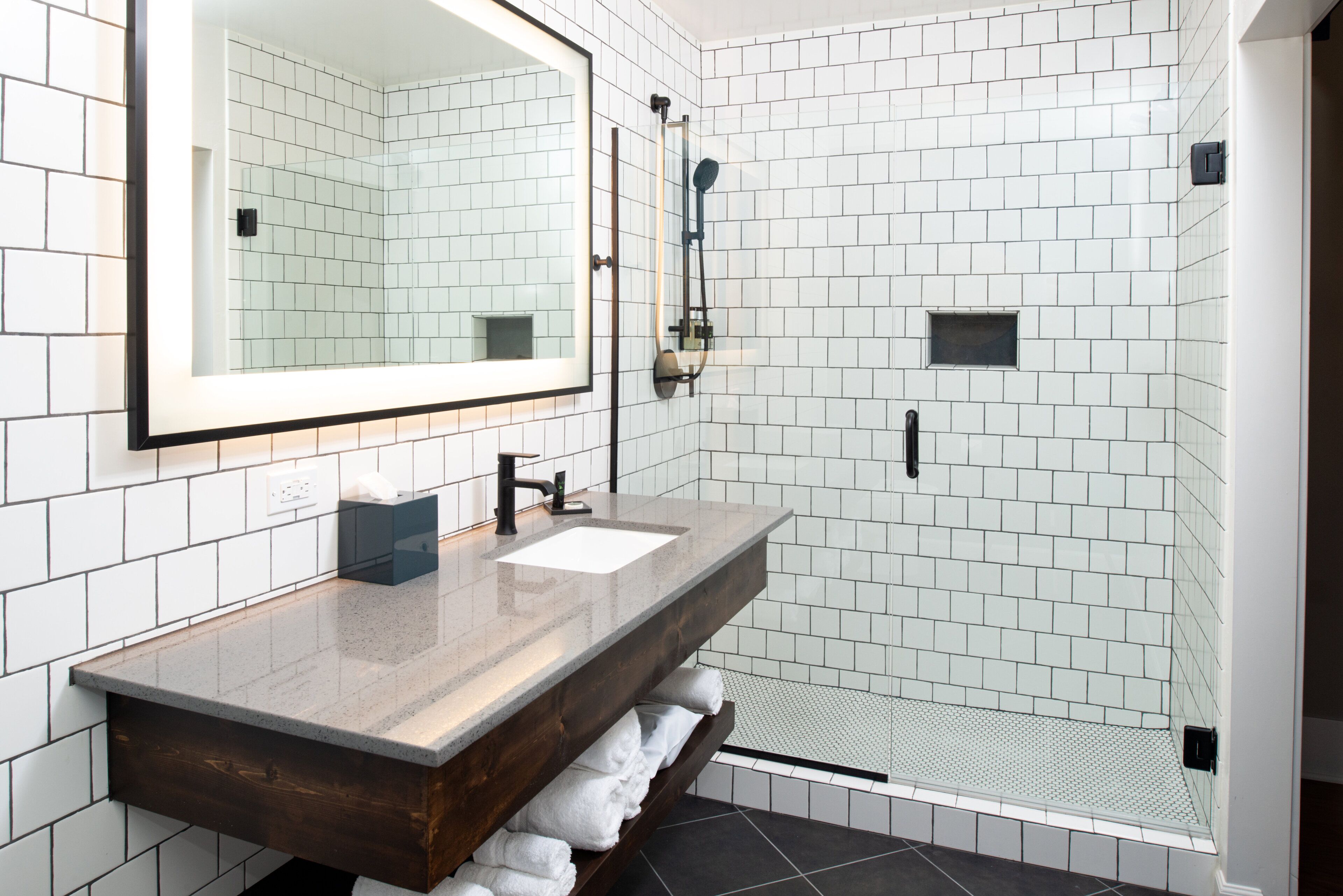 Une salle de bain moderne avec un grand miroir, un lavabo et un espace douche aux carreaux blancs.