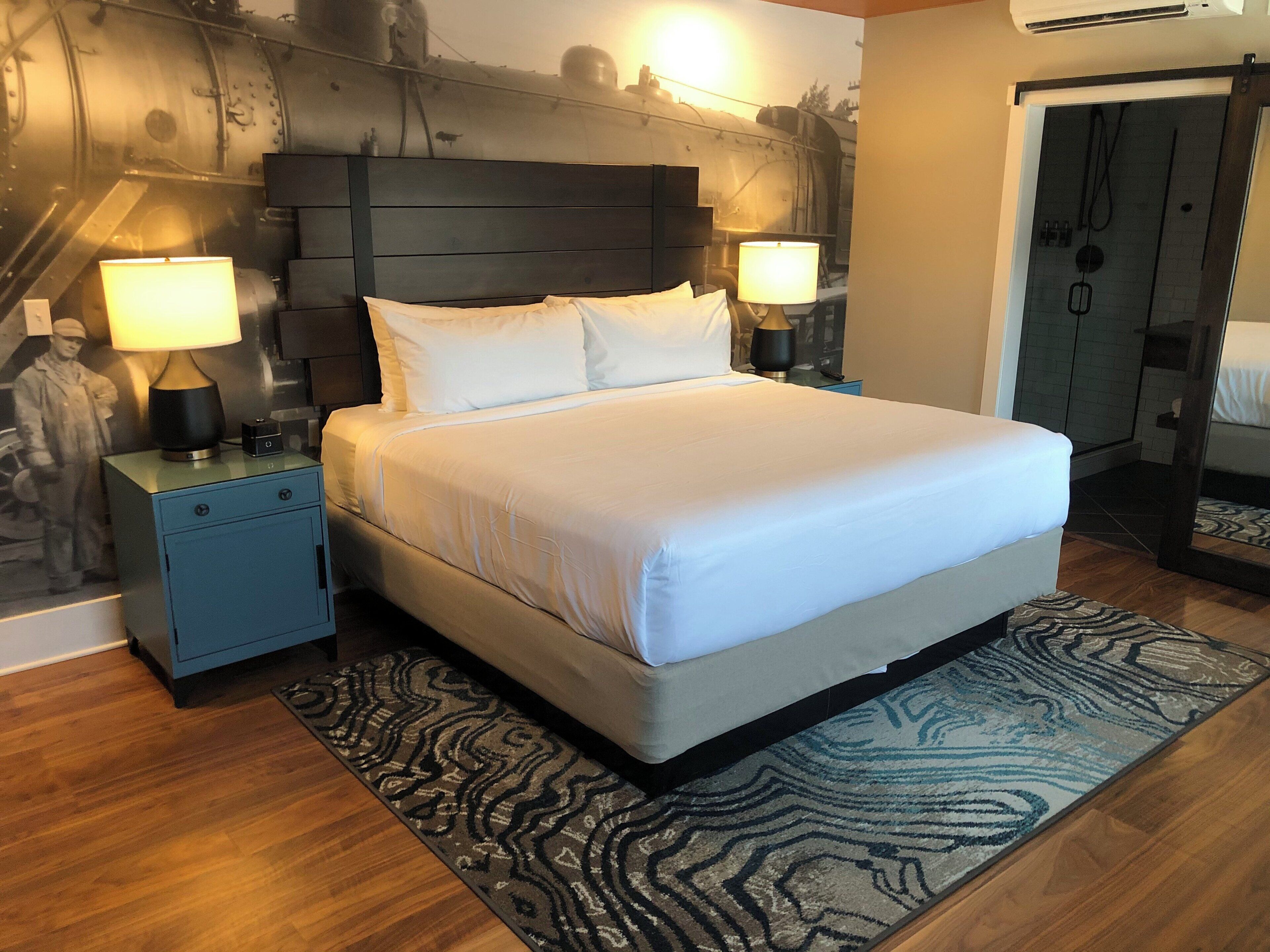 A hotel room with a large bed, two bedside tables with lamps, a patterned rug, and a wall with a mural.