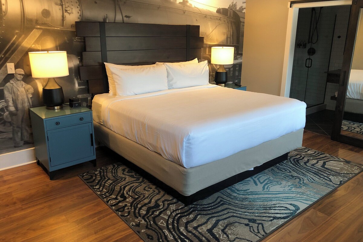 A hotel room with a large bed, two bedside tables with lamps, a patterned rug, and a wall with a mural.