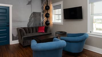 Una sala de estar con un sofá, dos sillones, una mesa de centro, un televisor y un mural en la pared.