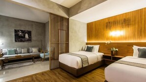 A modern hotel room with two beds, a wooden headboard, a large window, and a grey sofa. - Kuta Legian Villa (Kuta)