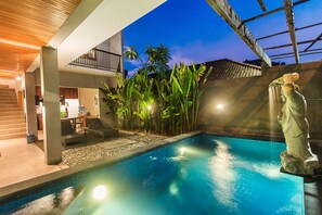 Una piscina con una statua, circondata da piante e un edificio moderno con un balcone.
