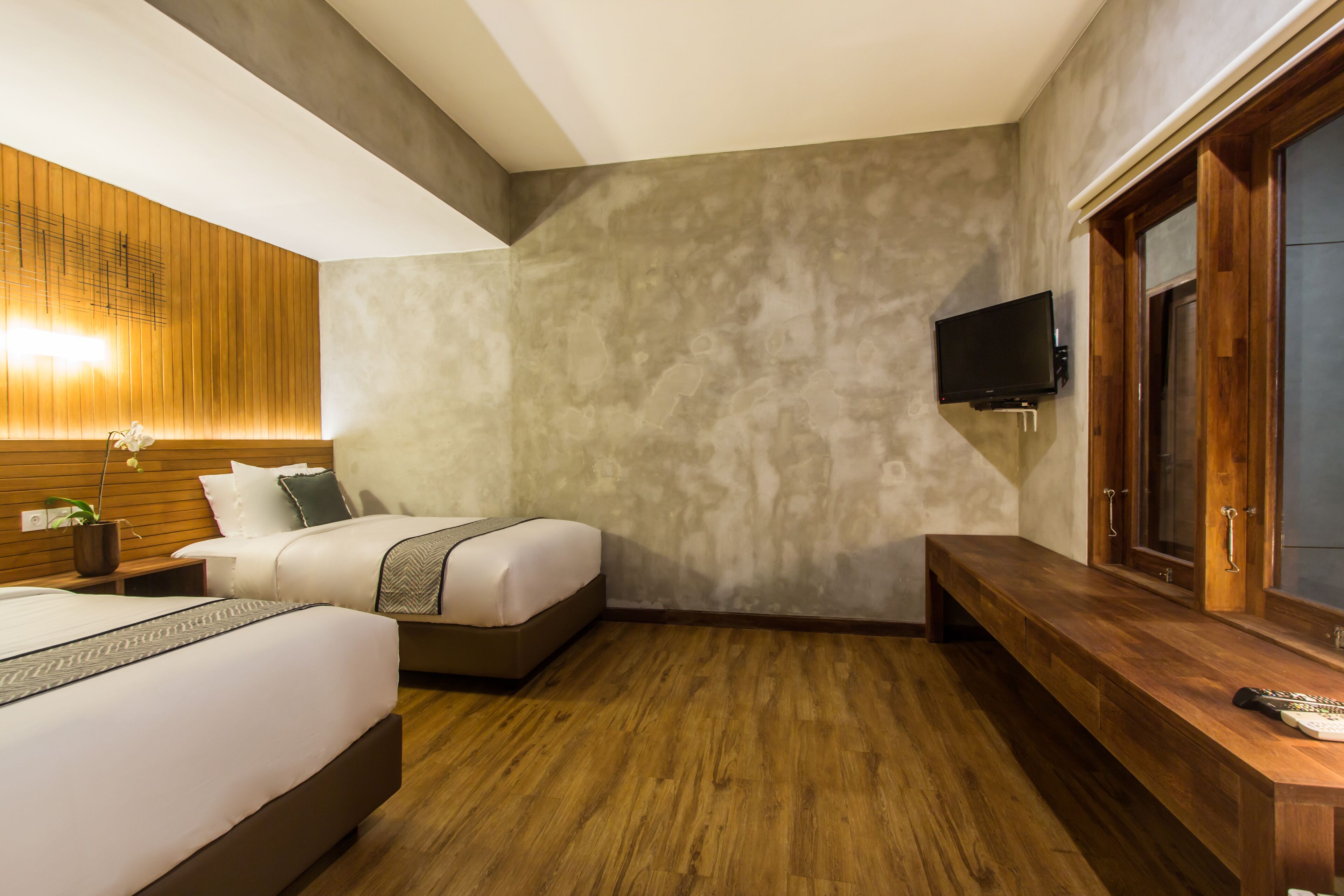 Una habitación de hotel moderna con dos camas, un banco de madera, un televisor montado en la pared y un armario espejo grande.