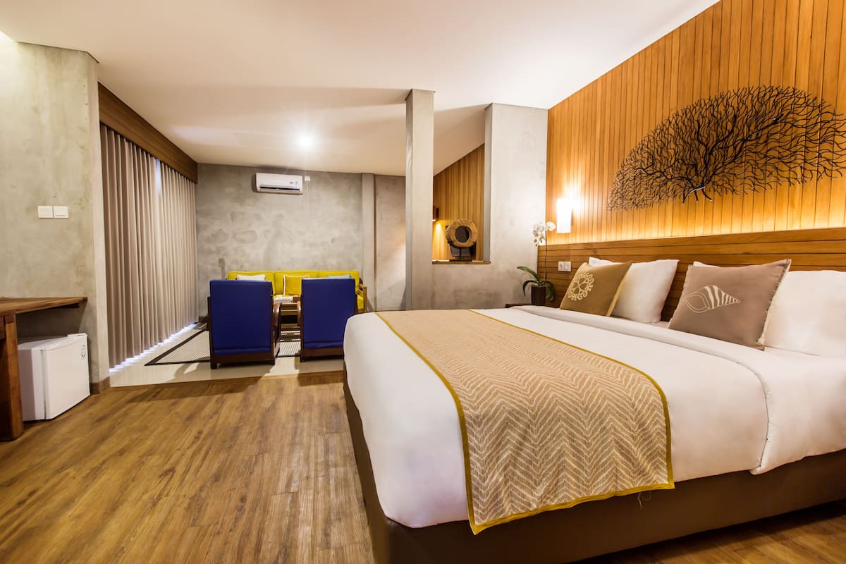 A hotel room with a large bed, a desk with a chair, a small table, and a decorative wall piece.