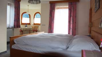 Een slaapkamer met een houten bed, twee ramen met gordijnen, een tafel met stoel en een hanglamp.