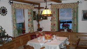 Ein Essbereich mit Tisch für vier Personen, Holzsesseln, einer Bank und einem Fenster mit floralem Vorhang.