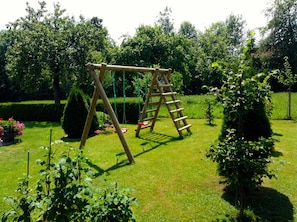 A wooden swing set in a well-maintained garden with hedges and flowering plants.