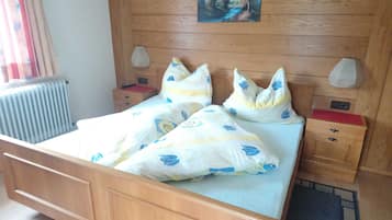 A wooden bed with a headboard, two bedside tables with lamps, a radiator, and a painting on the wall.