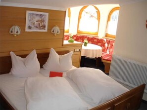 A hotel room with a bed, a small table, a bench, and a radiator. - Double room 2 - Haus Waldheim (Oetz)