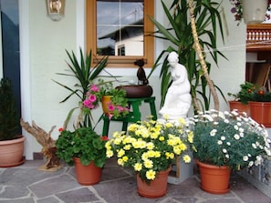 A potted plant arrangement outside a building with a window, a statue, and a green stool. - Double room 3 - Haus Waldheim (Oetz)