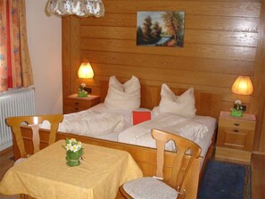 Ein Doppelzimmer mit zwei Betten, einem Holz-Kopfteil, Nachttischen mit Lampen, einem kleinen Tisch mit Blumenvase und einem Bild an der Wand.
