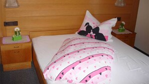 Un dormitorio con cabecera de madera, cama con ropa de cama rosa y blanca, dos mesitas de noche con lámparas y un pequeño adorno en una de ellas.