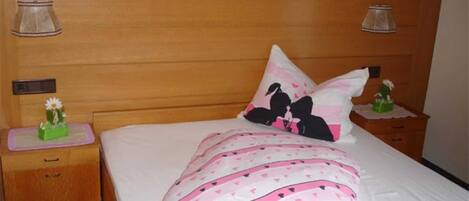 A bedroom with a wooden headboard, a bed with pink and white bedding, two bedside tables with lamps, and a small decorative item on one table.