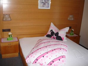 Ein Schlafzimmer mit einem Holz-Kopfteil, einem Bett mit rosa und weißer Bettwäsche, zwei Nachttischen mit Lampen und einem kleinen dekorativen Gegenstand auf einem Tisch.