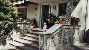 Una escalera de piedra que lleva a una puerta, rodeada de plantas en macetas y una estatua.