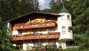 A multi-story building with wooden balconies, a tower-like structure, and a garden area with flowers.