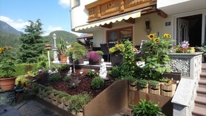 A building with a garden in front, a balcony with wooden railings, and a mountain in the background. - Double room 3 - Haus Waldheim (Oetz)