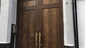 A large wooden double door with brass handles, set in a white and black exterior wall. - StayPlus Central Apt Balcony (Oslo)