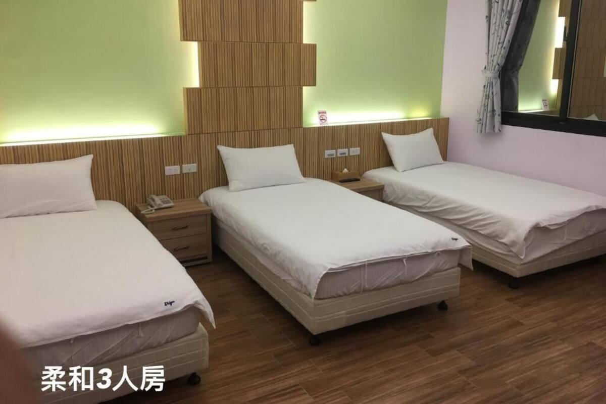 A hotel room with three single beds, a wooden headboard, a bedside table with a phone, and a mirror.