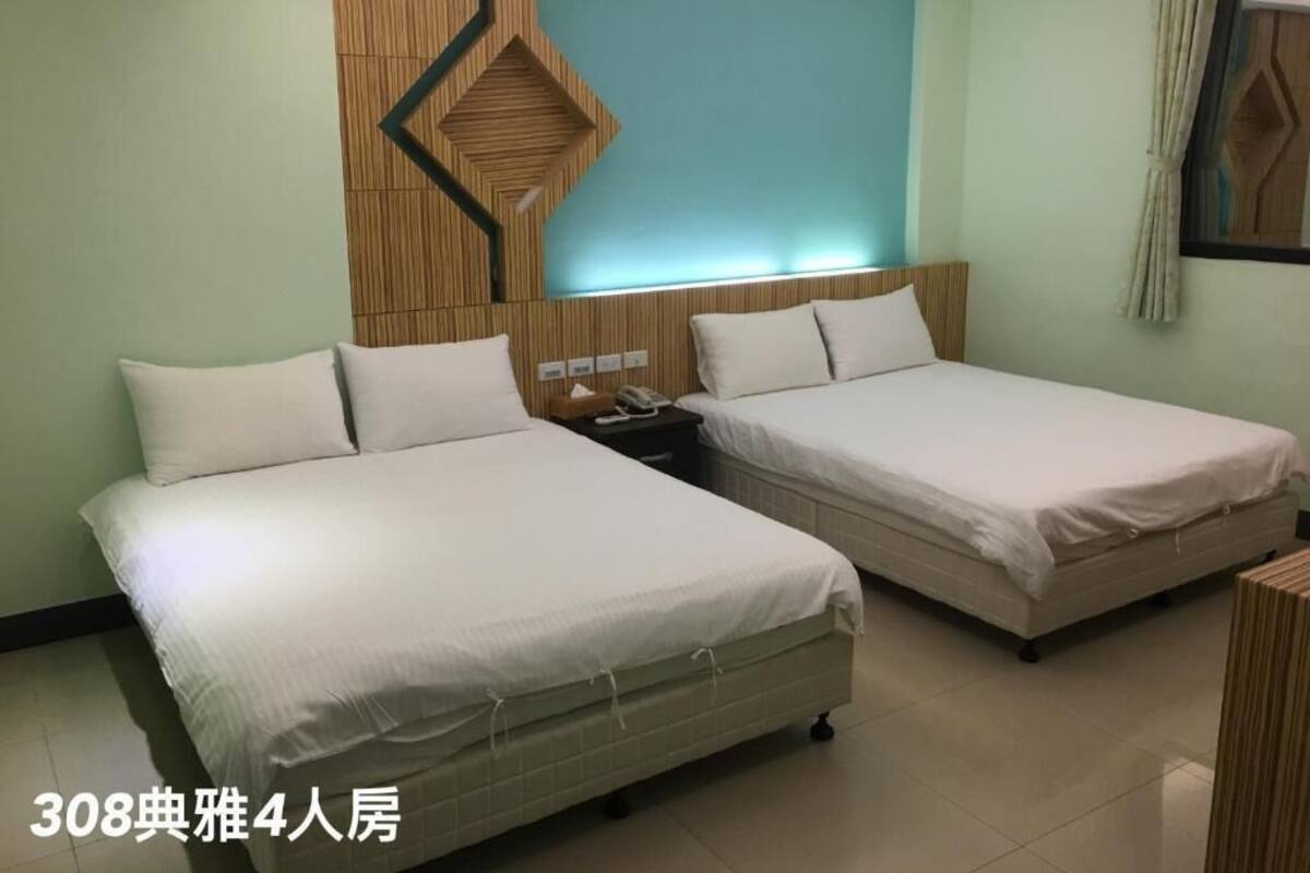 A 4-person room with two beds, a wooden headboard, a nightstand, and a wall-mounted light fixture.