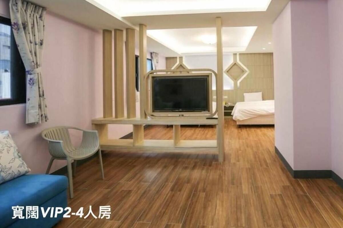 A modern hotel room with a TV mounted on a wooden structure, a bed, a blue sofa, and a chair.