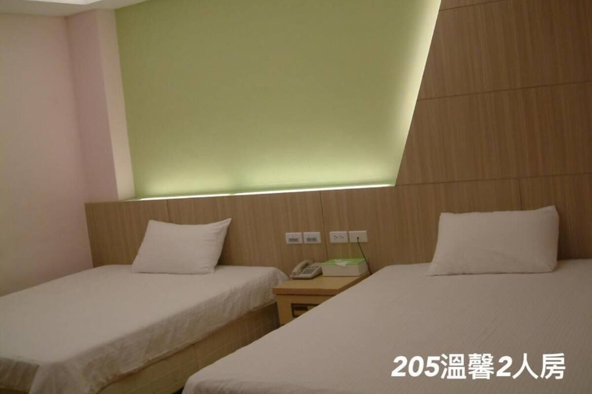 A hotel room with two beds, a bedside telephone, and a wall-mounted light fixture.