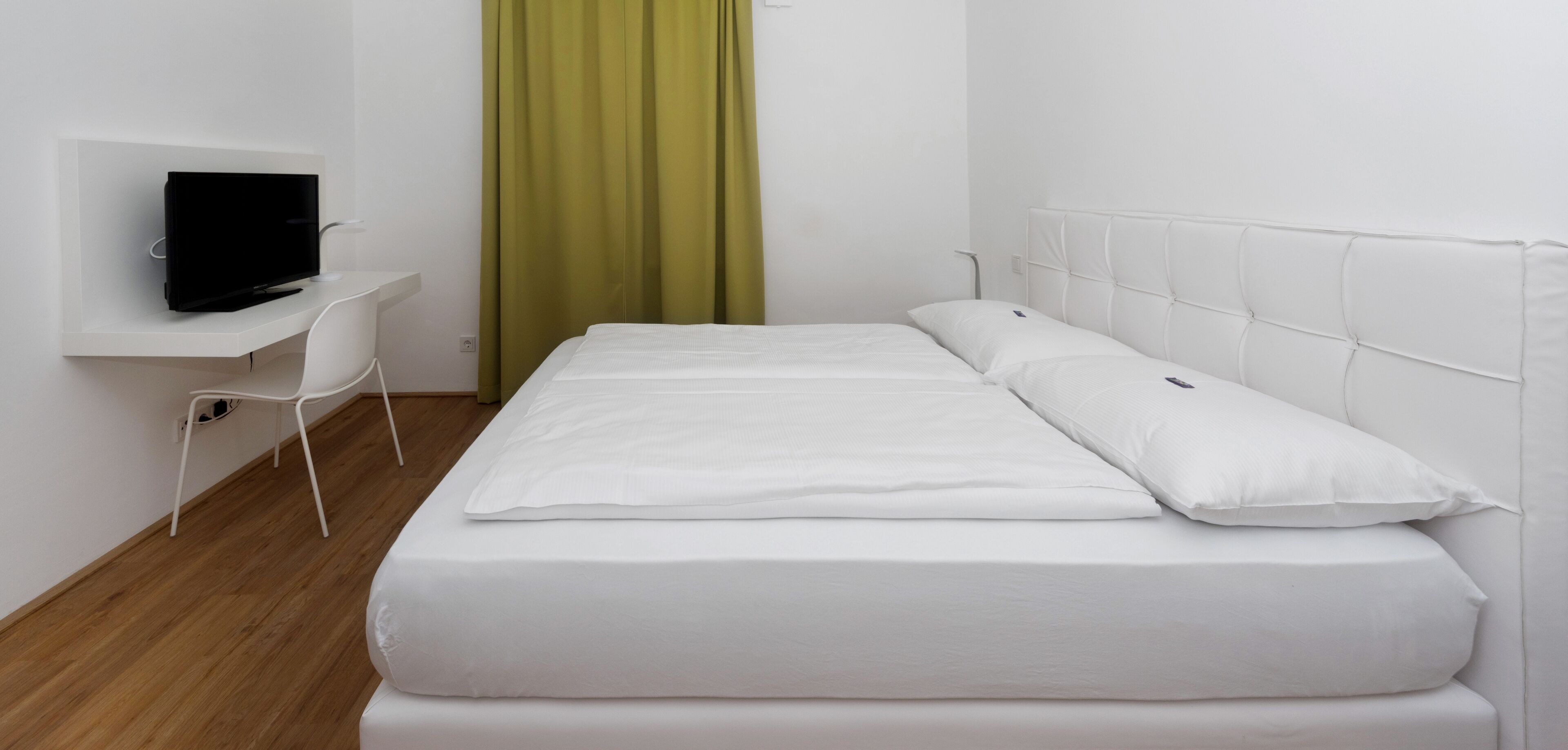 Ein Hotelzimmer mit einem Bett, einem Fernseher auf einem weißen Schrank und einem grünen Vorhang.