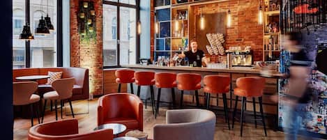 Una zona de bar con sillas rojas, un barman y una pared llena de discos de vinilo.