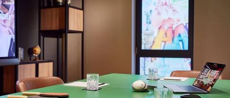 Un salón de conferencias con una mesa verde, computadoras portátiles, un proyector y un amplio ventanal.
