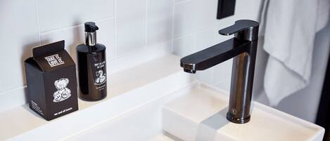 Un baño moderno con un lavamanos blanco, un grifo negro y dos botellas de artículos de aseo sobre el mostrador.