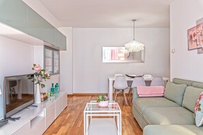 A modern living room with a sofa, a coffee table, a TV, and a dining area with chairs and a table. - Cálido apartamento con piscina en Barcelona. (Ripollet)