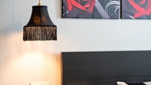 Ein ordentlich bezogenes Bett mit dunkelbrauner Kopfteil, ein Nachttisch mit schwarzer Lampe und eine rote Rose darauf.