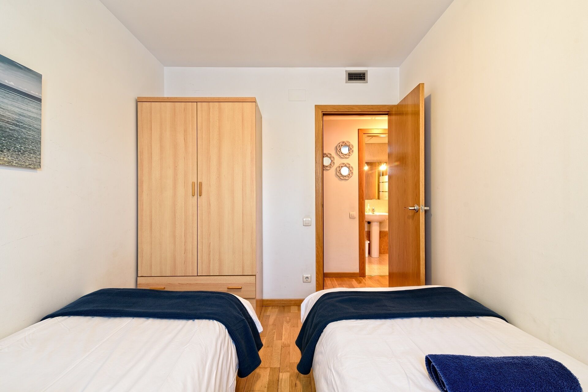 Een slaapkamer met twee bedden, een houten garderobe en een zichtbare badkamer door een open deur.