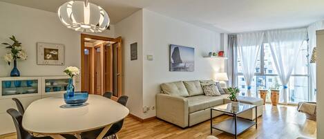 Una sala de estar moderna con una mesa redonda de comedor, un sofá color beige y una mesa de centro. Hay un cuadro en la pared y un jarrón con flores sobre la mesa.