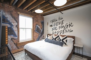 Una camera da letto con parete in mattoni, un'ampia finestra e una citazione motivazionale sulla parete.
